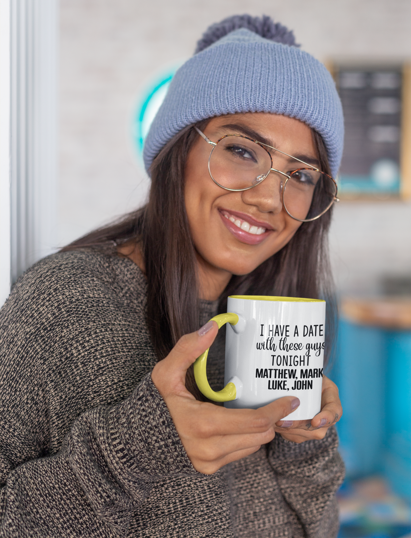 Person wearing a blue beanie and glasses, holding a mug with text.