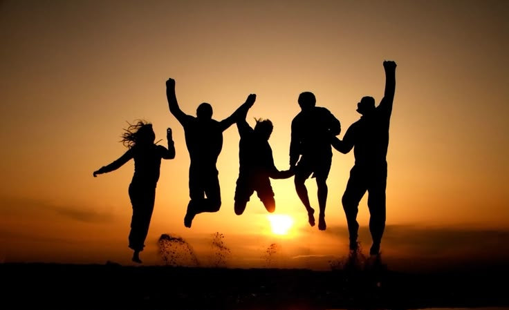Silhouettes of people jumping in the air with a sunset reflection on water.