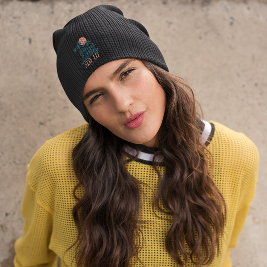 Woman wearing a black beanie and yellow sweater against a concrete wall.