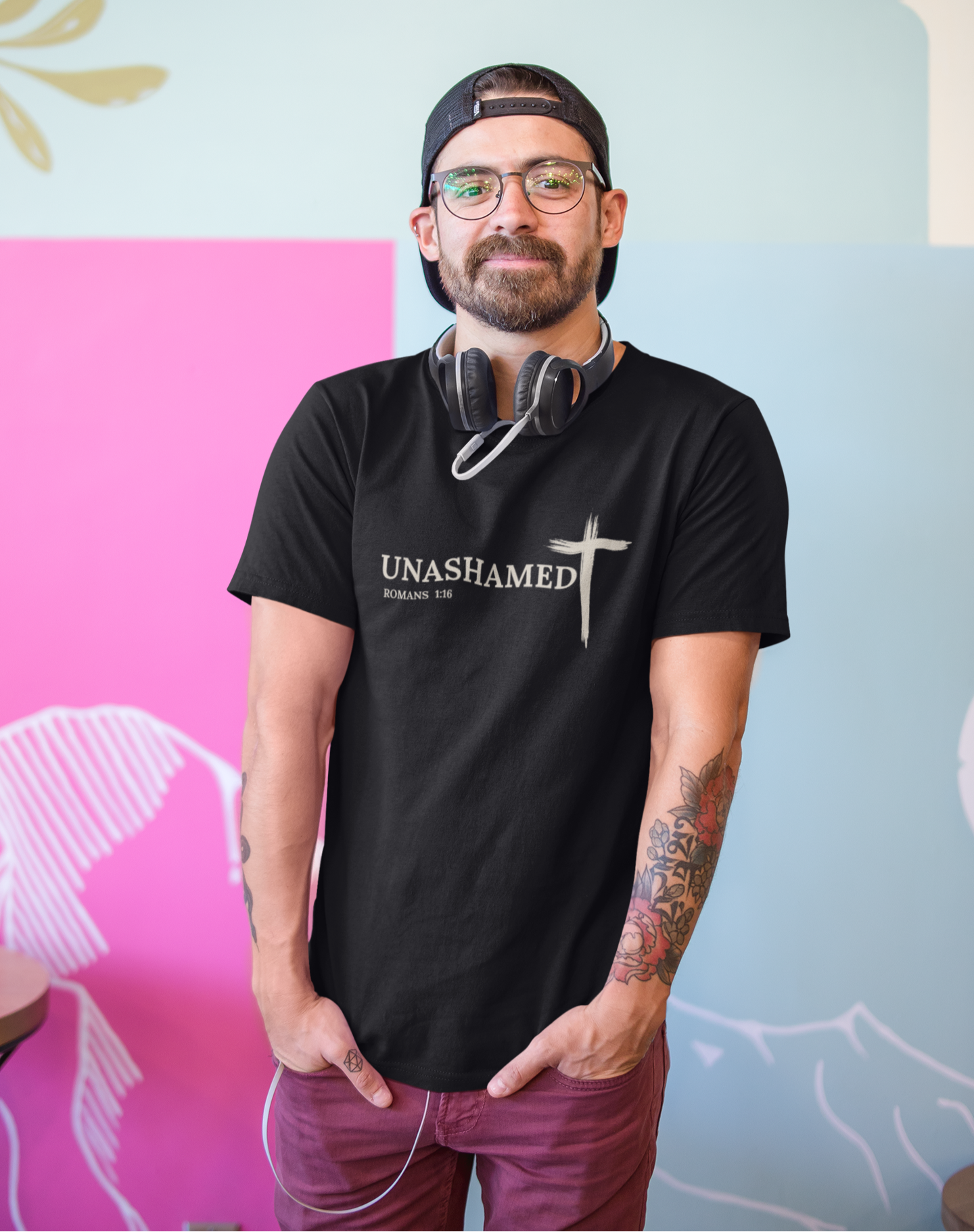 Man wearing a black t-shirt with 'UNASHAMED' text, standing against a colorful wall.