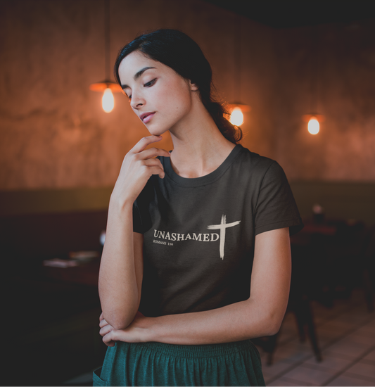 Woman wearing a black t-shirt with 'UNASHAMED' text in a dimly lit room.