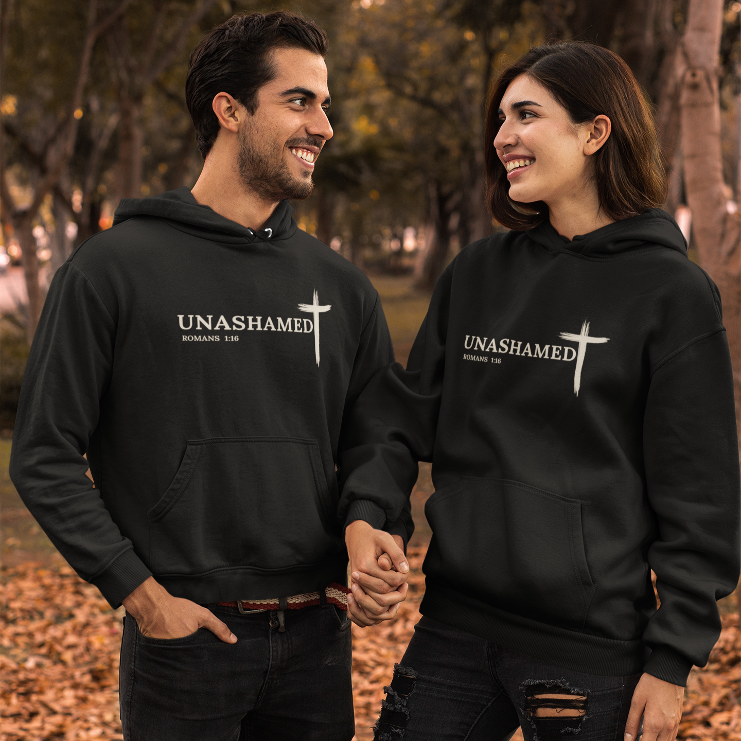 Two people wearing black hoodies with 'UNASHAMED' text, standing outdoors.